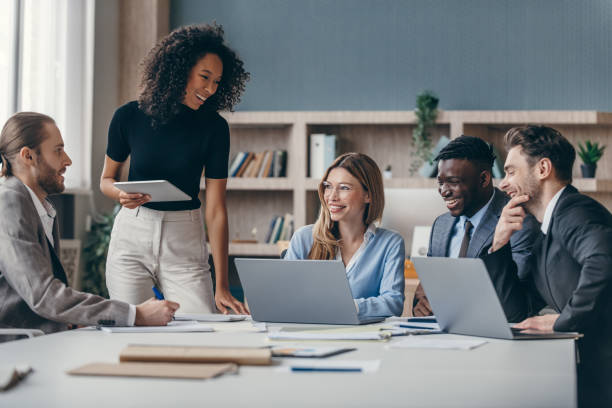 A diverse team smiling and collaborating around a meeting table with laptops